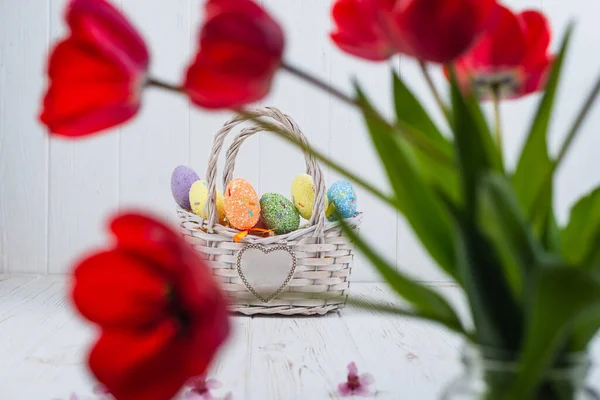 Mnohobarevné velikonoční vejce v košíku na bílém dřevěném pozadí — Stock fotografie