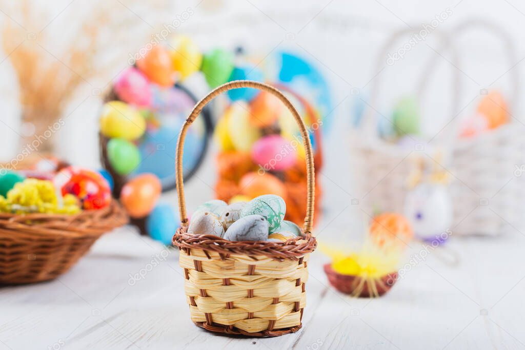 Multi-colored Easter eggs in a basket on a white wooden background