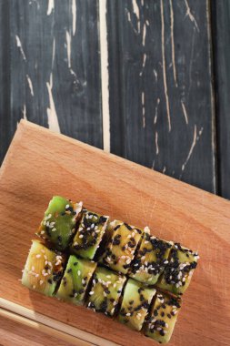 Koyu ahşap arka planda tahta üzerinde somon balıklı suşi.