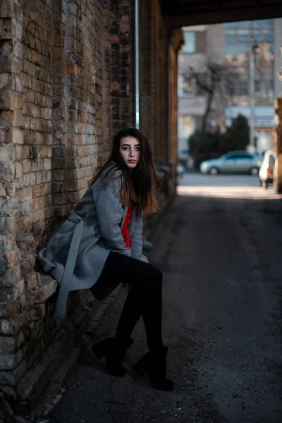 Girl in a red blouse and a gray cardigan on the background of the old brick wall — Stock Photo, Image