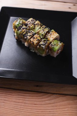 Kare siyah bir tabakta somon balığı ve ahşap bir arka plan.