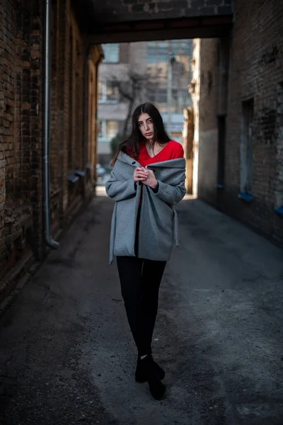 Girl in a red blouse and a gray cardigan on the background of the old brick wall — Stock Photo, Image