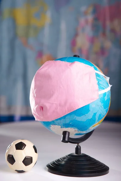 Globe in a medical mask with a soccer ball. The concept of canceling football matches due to coronavirus