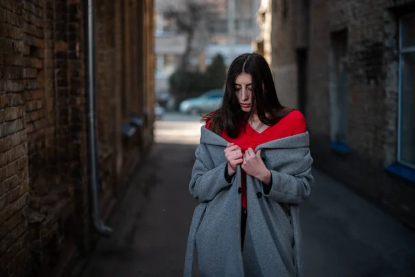 Girl in a red blouse and a gray cardigan on the background of the old brick wall — Stock Photo, Image