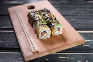 Koyu ahşap arka planda tahta üzerinde somon balıklı suşi.