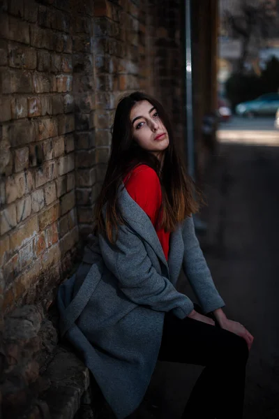 Chica en una blusa roja y un cárdigan gris en el fondo de la vieja pared de ladrillo —  Fotos de Stock