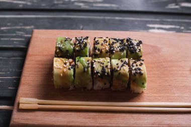 Koyu ahşap arka planda tahta üzerinde somon balıklı suşi.