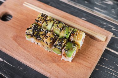 Koyu ahşap arka planda tahta üzerinde somon balıklı suşi.