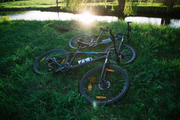 Два спортивных велосипеда на траве возле реки на закате солнца — стоковое фото