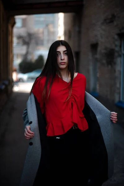 Дівчина в червоній блузці і сірий кардиган на тлі старої цегляної стіни — стокове фото