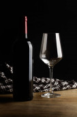 Láhev červeného vína a sklenici na dřevěném stole v tmavém pozadí