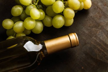 Bir şişe beyaz şarap ve bir demet yeşil üzüm.