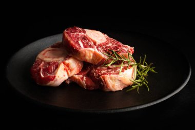 Siyah bir tabakta çiğ osso buco ve koyu bir arka plan.