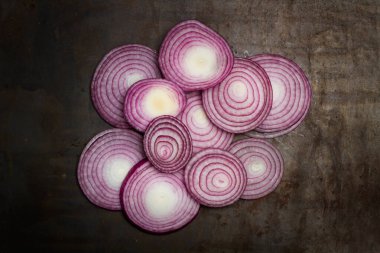 Üstten bakıldığında paslı metal bir masada mor soğan dilimleri.