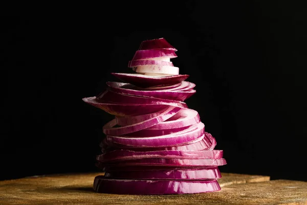 A heap of sliced purple onion on a wooden table on a dark background