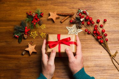 Tahta bir masada elinde noel hediyesi tutan bir adam.