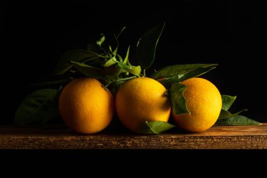 Koyu arkaplanda, tahta bir masada üç portakal.