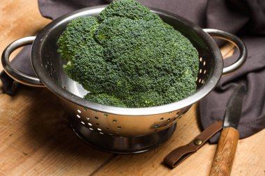 Broccoli in a strainer on a wooden table clipart