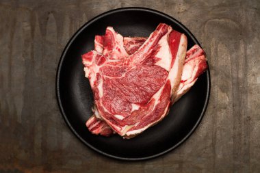 Paslı metal bir masada siyah bir tabakta iki biftek.