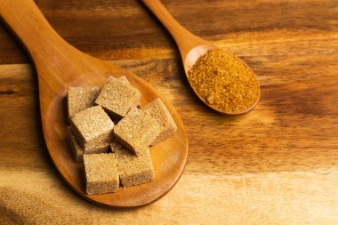 Tahta kaşıkta kahverengi şeker küpleri ve kahverengi şekerli ahşap kaşık.