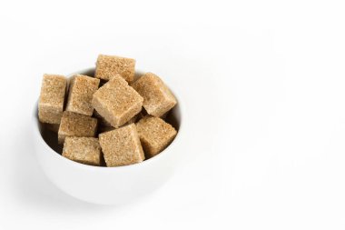 Beyaz arka planda beyaz bir kasede kahverengi şeker küpleri