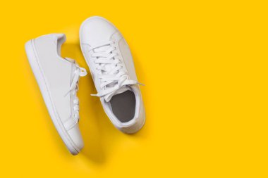 Sarı arka planda beyaz bir çift spor ayakkabı.