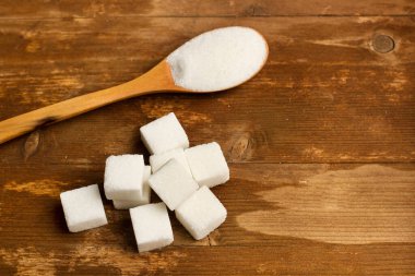 Tahta masada küp şekerler ve tahta kaşıkta beyaz şeker.