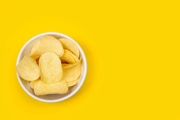 Sarı arka planda seramik bir kasede patates cipsi.