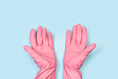 Açık mavi arka planda pembe lastik eldivenli eller