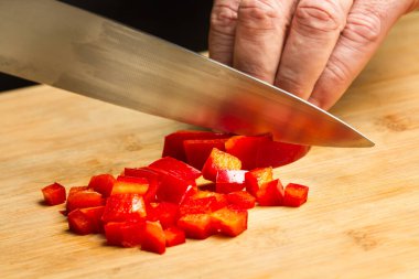 Ahşap mutfak tahtasına kırmızı dolma biber kesen bir adam.