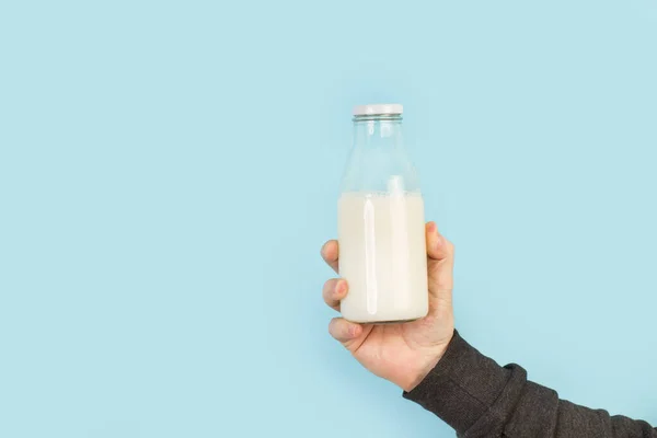 男の手は薄い青の背景にミルクのボトルを保持 — ストック写真