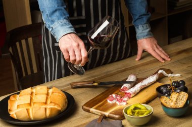Aperatifler ve elinde bir bardak kırmızı şarapla masada duran bir adam.