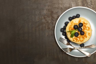 Üzerinde yaban mersini olan krepler, gri bir tabakta, paslı metal bir masanın üstünde, en üstte. 