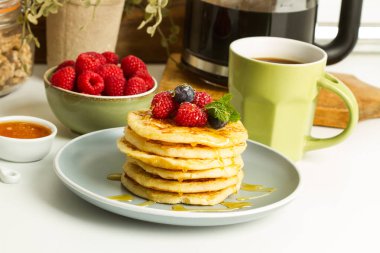 Böğürtlenli krep ve gri tabakta bal ve mutfak tezgahında bir fincan kahve.