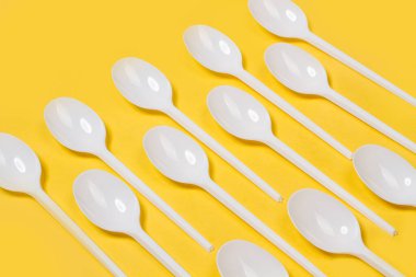 Sarı arka planda tek kullanımlık plastik kaşıklar.