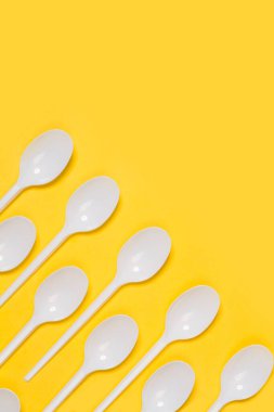 Sarı arka planda tek kullanımlık plastik kaşıklar.