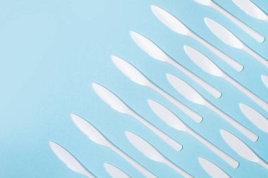 Açık mavi arka planda tek kullanımlık beyaz plastik bıçaklar.