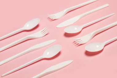 Tek kullanımlık beyaz plastik çatal bıçak takımı pembe arka planda, üstte.
