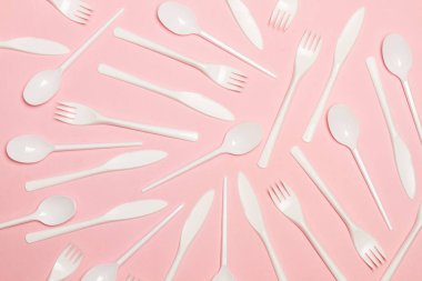Tek kullanımlık beyaz plastik çatal bıçak takımı pembe arka planda, üstte.