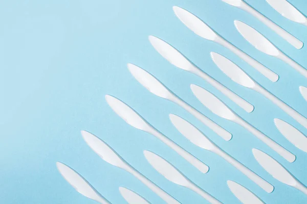 Disposable white plastic knifes on a light blue background