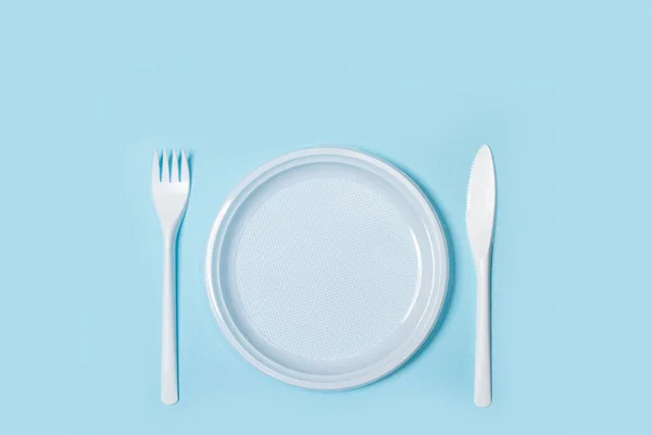 Disposable plastic white cutlery and plate on a light blue background in a top view