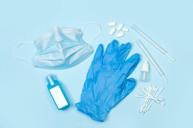 Ameliyat maskesi, tıbbi eldivenler ve açık mavi arka planda bir şişe alkol.