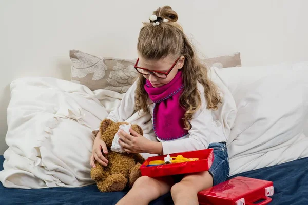 Niña enferma en gafas, cura a su oso de peluche enfermo —  Fotos de Stock