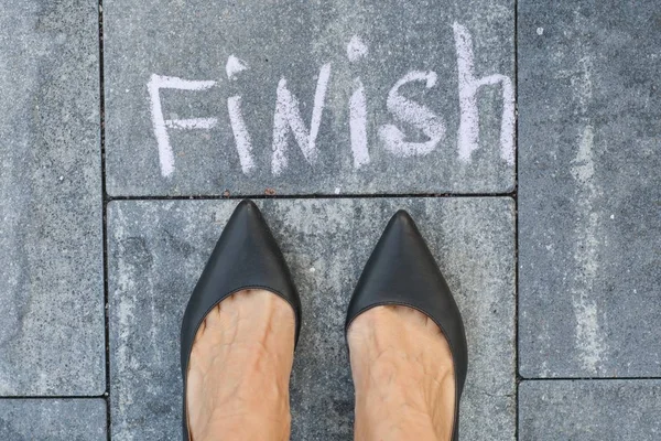 Los pies de una mujer en zapatos clásicos negros antes de la palabra finis —  Fotos de Stock