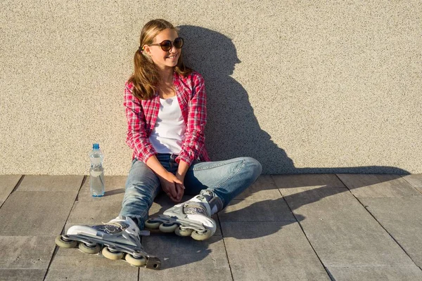 Jovem sorrindo menina legal calçado em patins, senta-se no sidewa — Fotografia de Stock