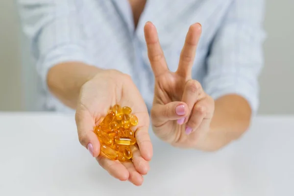 Manos de una mujer sosteniendo aceite de pescado Omega-3 cápsulas y mostrando v — Foto de Stock