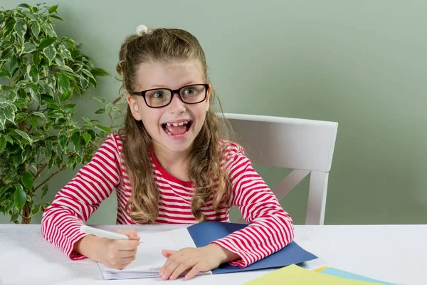 Una colegiala en gafas escribiendo algo en copybook a — Foto de Stock