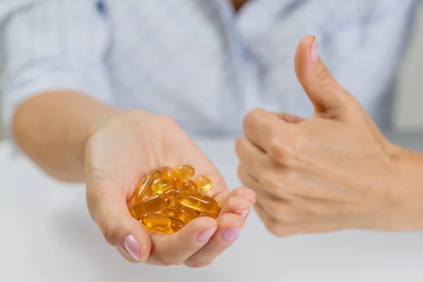 Hand of a woman with fish oil Omega-3 capsules. Shows thumbs up — Stock Photo, Image