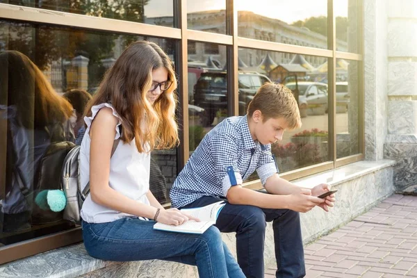 Dzieci młodzieży, czytając książkę i za pomocą smartfona. — Zdjęcie stockowe