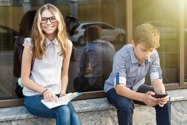 A niños adolescentes, leyendo libros y usando teléfonos inteligentes . —  Fotos de Stock
